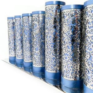 Menorah of blue metal rolls wrapped with metal cutouts of pomegranates
